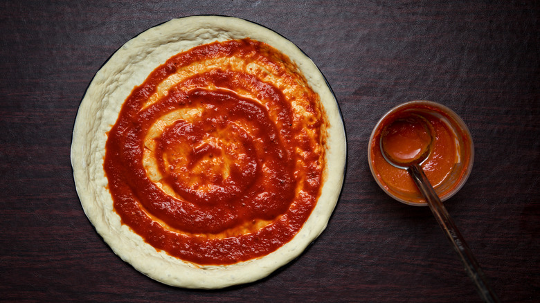 Top view of unbaked pizza dough spread with tomato pizza sauce