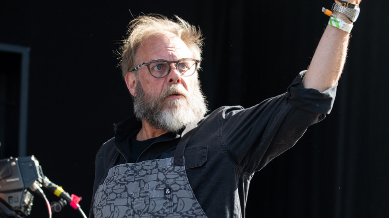 Alton Brown with his arm raised in the air and an apron on