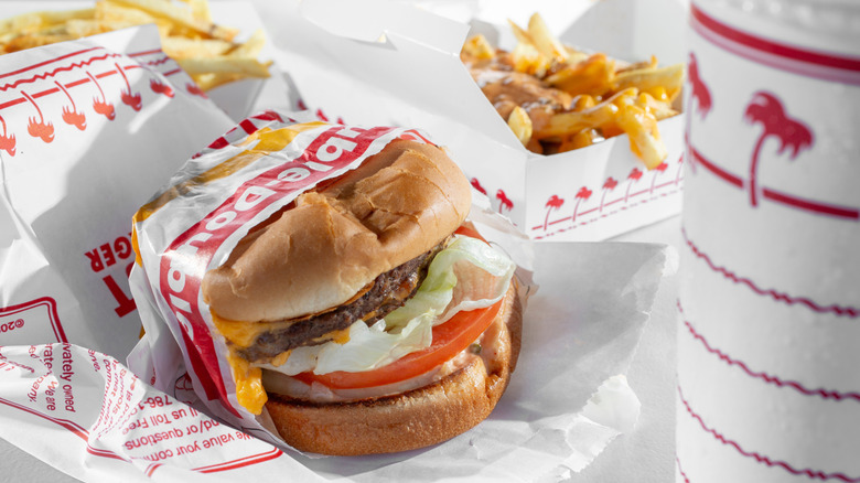 An In-N-Out burger in a paper wrapper with fries and a drink