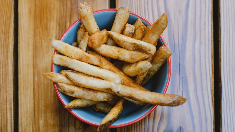 Aerial view of thick french fries in a small bowl on a wooden table.