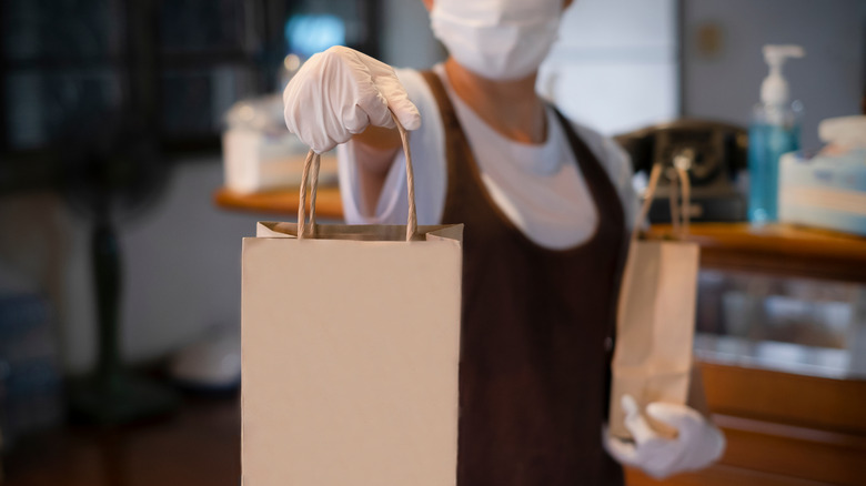 woman in mask and gloves hands over takeout bag