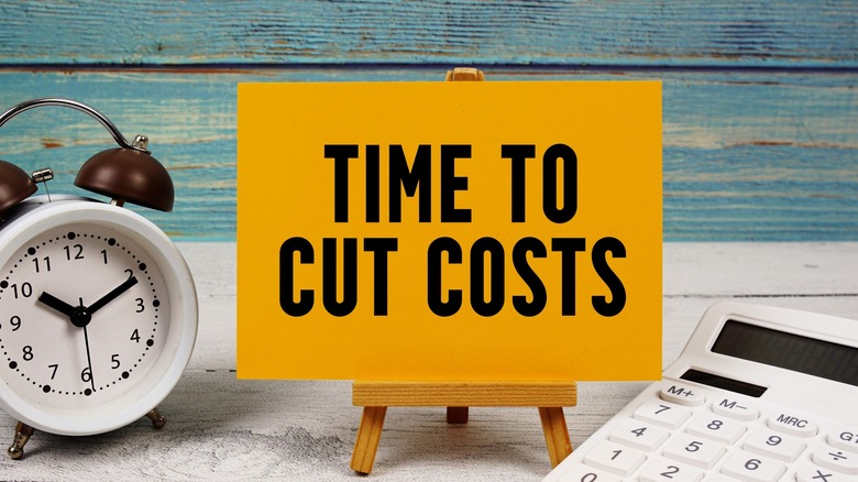 Time To Cut Costs text written on paper card with calculator and alarm clock on wooden background