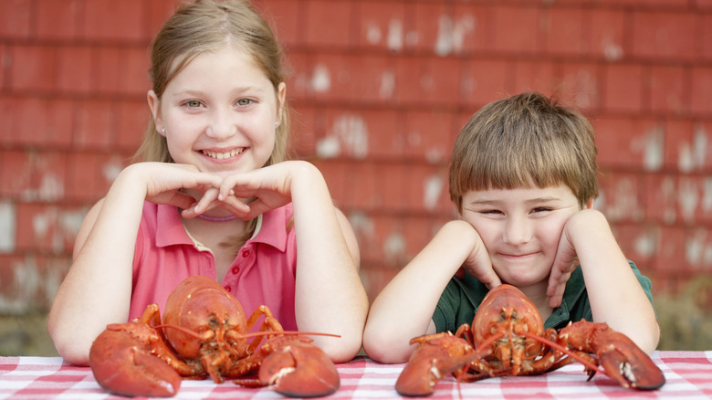 Two children pose with boiled lobsters on the table in front of them.