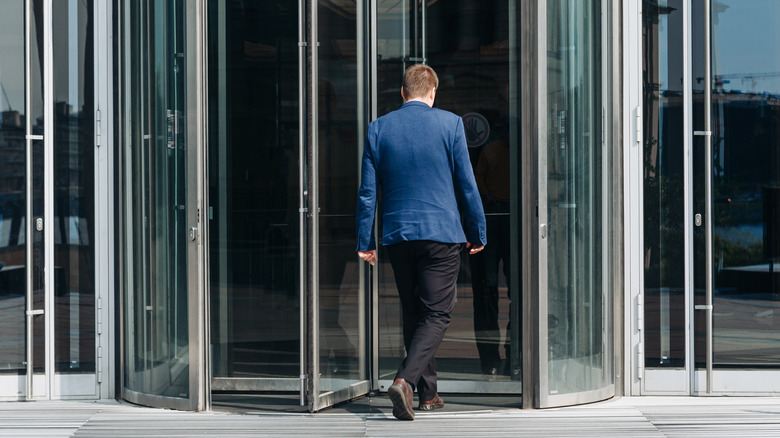 Man in a blue suit jacket exiting through a glass revolving door.