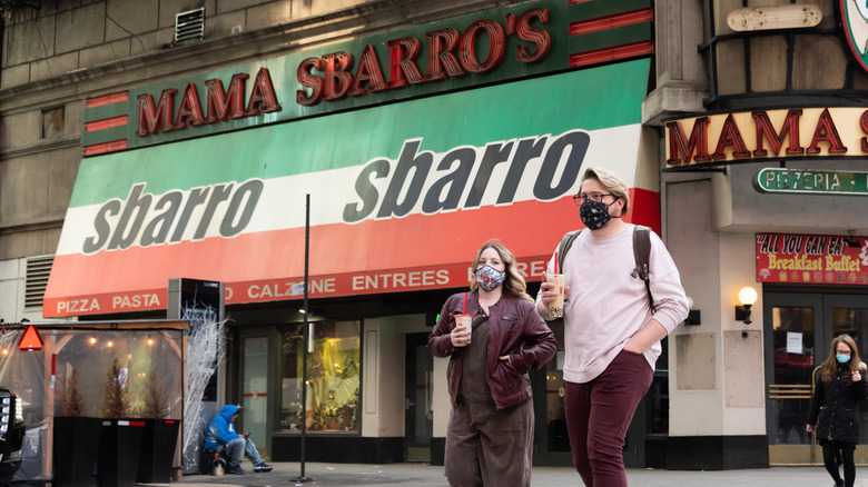 people walk past freestanding Sbarro in masks