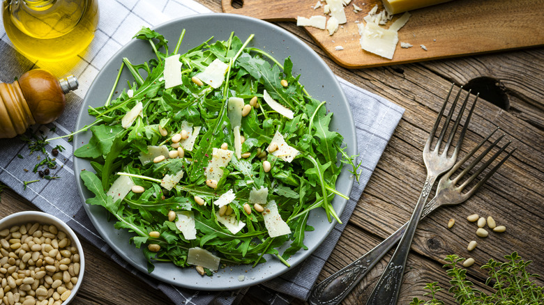 An arugula salad next to two forks and olive oil