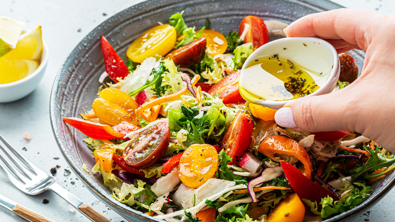 A hand pouring dressing onto a bowl of salad