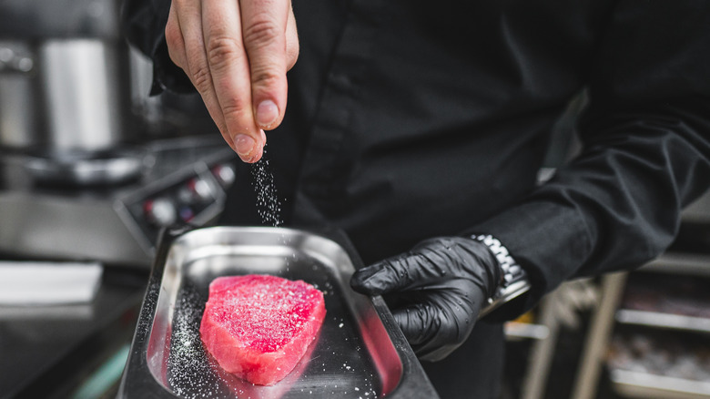 Hand seasons raw fish steak with salt