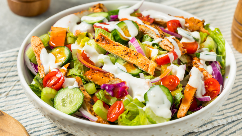 A bowl of mixed salad with vegetables, sliced chicken, and a creamy dressing