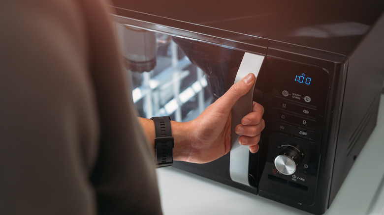 A hand opening a black microwave oven
