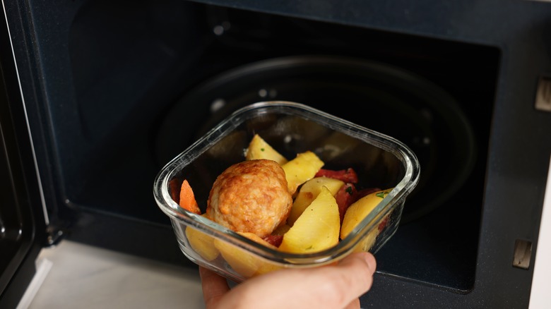 A glass container with food being put in a microwave