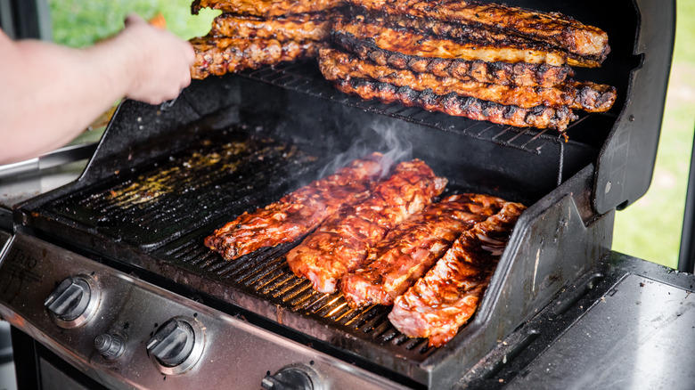 A person cooks ribs on a grill