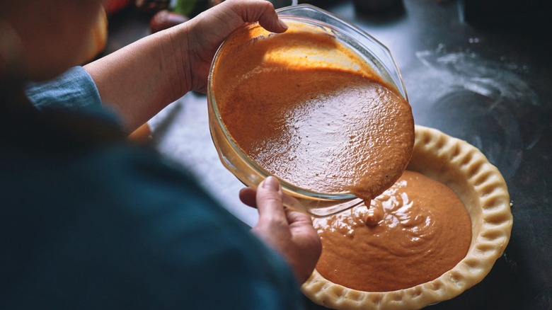 Person pouring pumpkin pie filling into pie crust