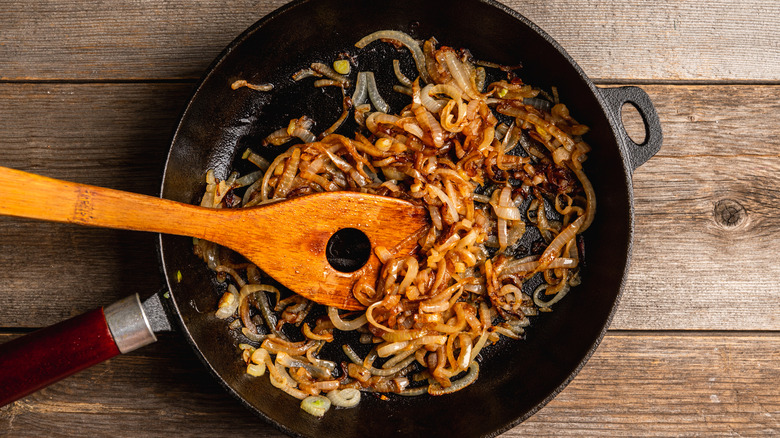 Caramelized onions in a cast iron pan on a wooden surface with wooden spatula.