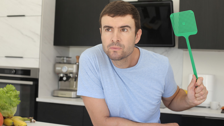 Man with flyswatter in kitchen