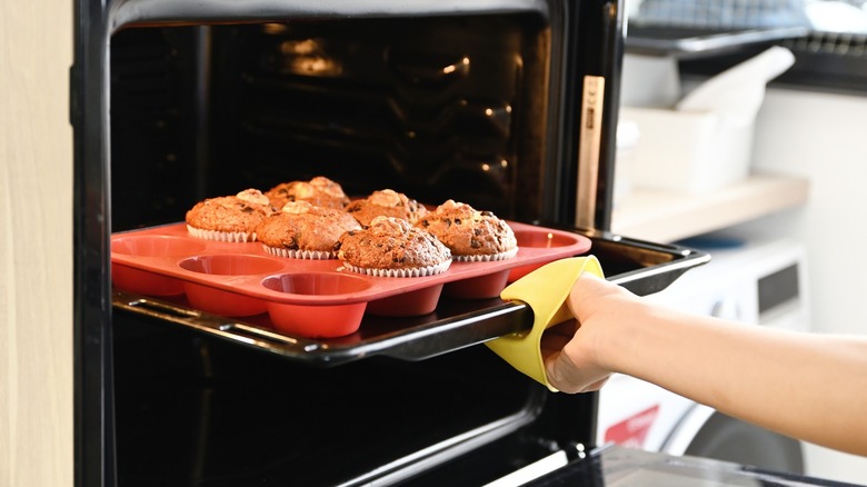 Person pulling muffins from oven