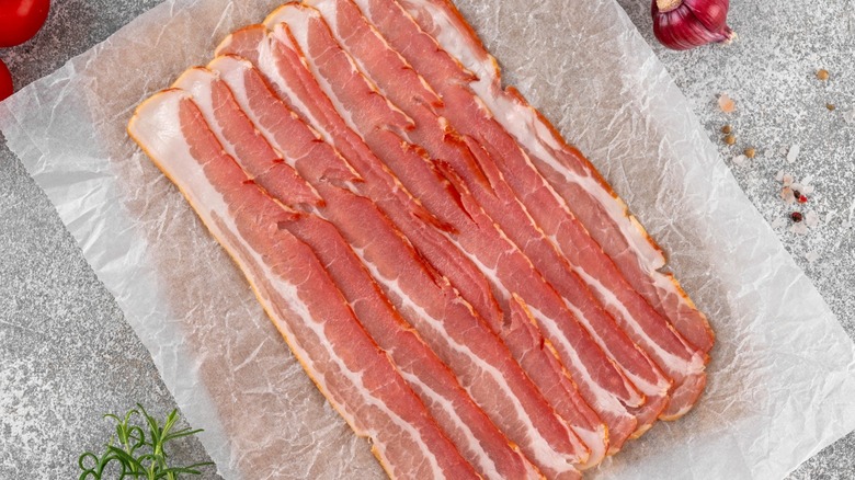 Raw bacon on paper sitting on wood board