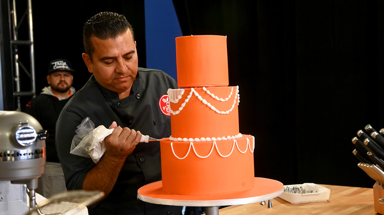 Buddy Valastro icing an orange three tiered cake