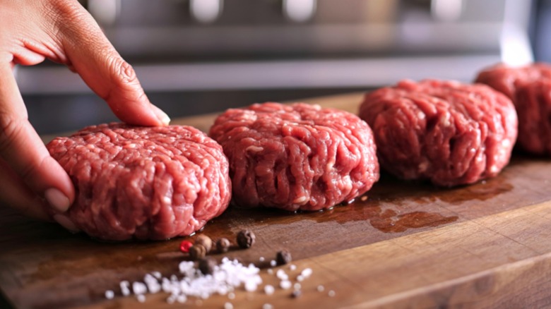 Hand placing raw burger patties on wood board