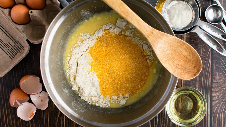 Ingredients for cornbread in mixing bowl with wood spoon on top