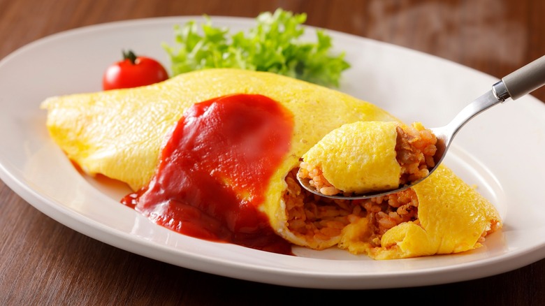 Spoon scooping up omelet filled with rice and topped with ketchup