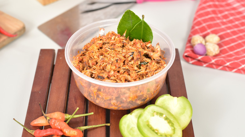 A small plastic bowl of spicy tuna salad, surrounded by peppers, tomatillos, and bay leaves