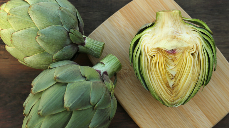 whole and cut artichokes on wooden cutting board