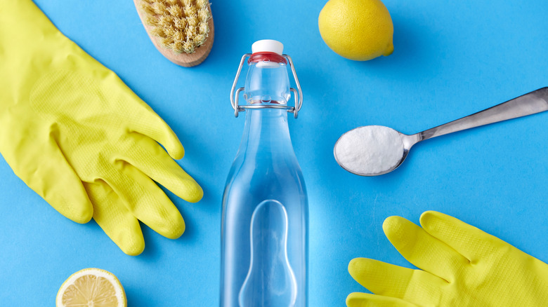 A bottle of vinegar, lemons, rubber gloves, washing soda and brush on blue background.