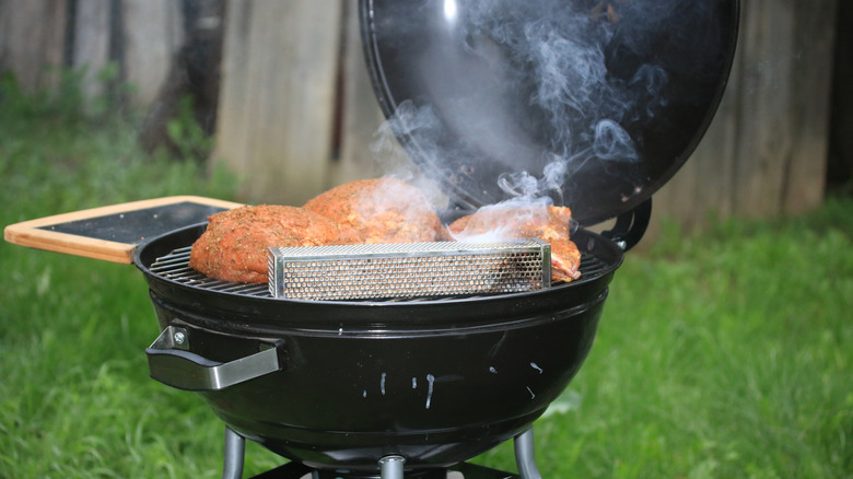 An open smoker with food cooking on the grill.