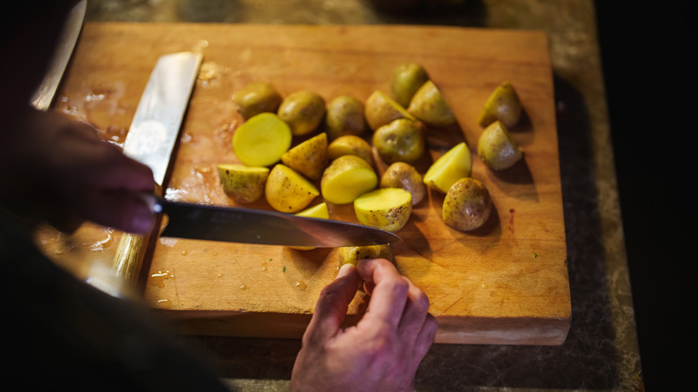 hands chopping potatoes on a wooden cutting board