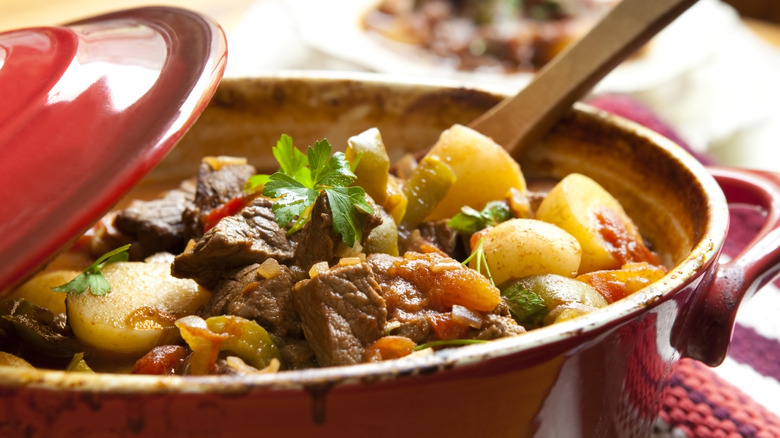 stew with chunks of meat, potatoes, and vegetables in a red pot
