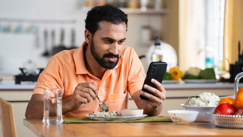 Man busy using phone while eating at the table