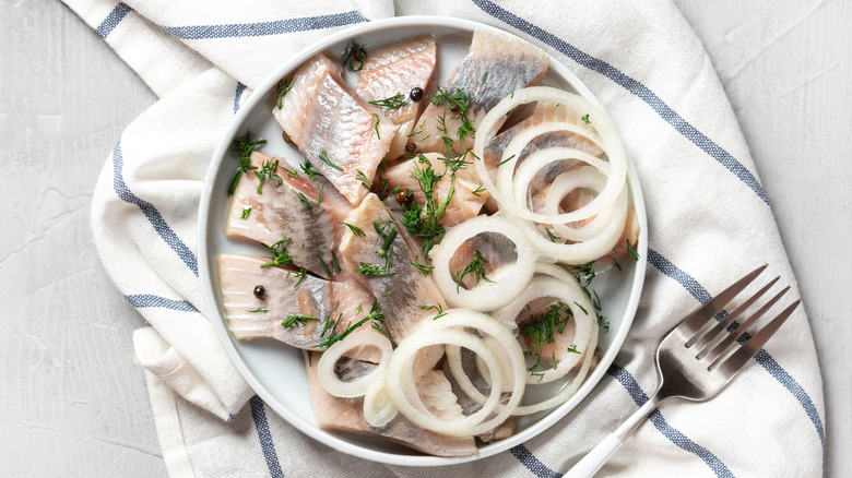 Pickled herring with onions and dill in a bowl next to a fork