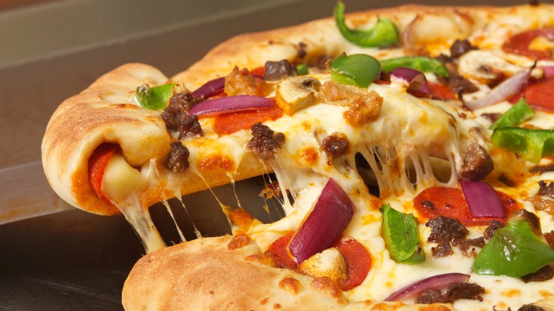 Slice of stuffed crust supreme pizza being lifted away from the rest of the pizza