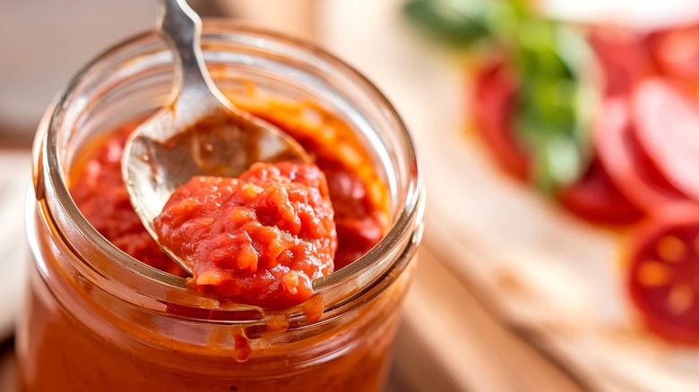 Spoon lifting pizza sauce out of glass jar