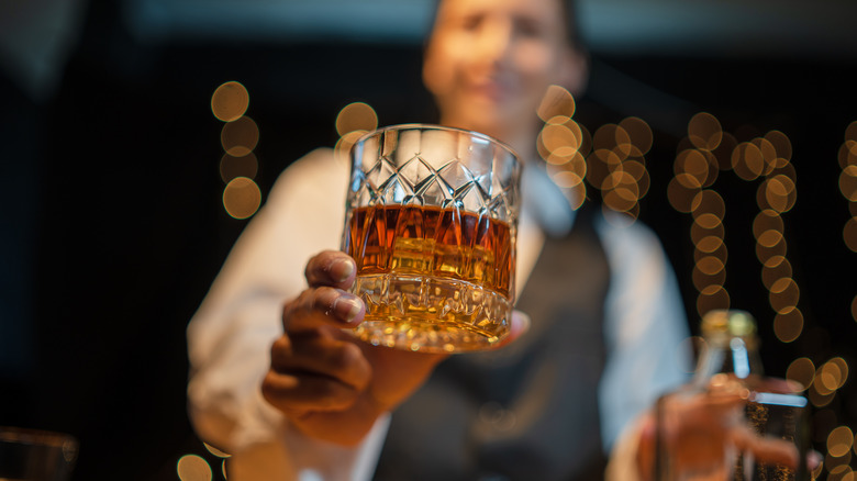 A glass of liquor being offered by a bartender with fuzzy background
