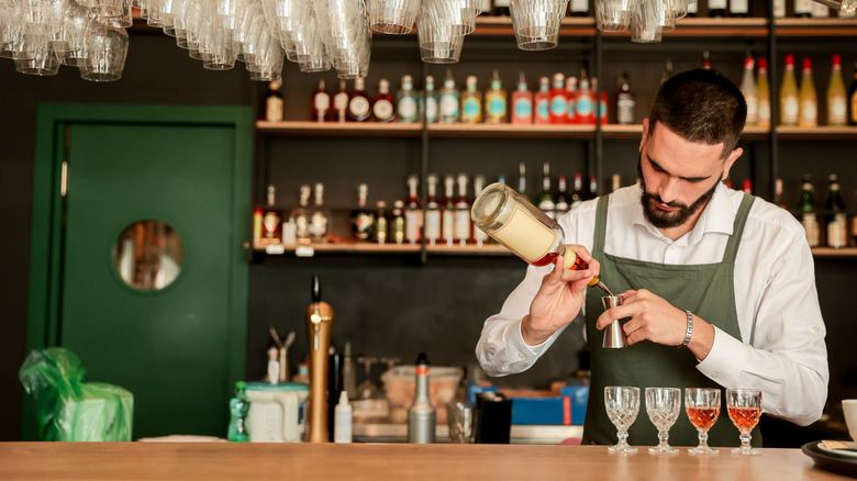 A male bartender pouring a series of drinks behind a bar