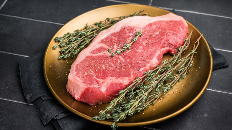 A raw New York strip steak and herbs