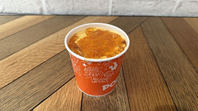 Popeyes macaroni and cheese in large cup on wooden surface.
