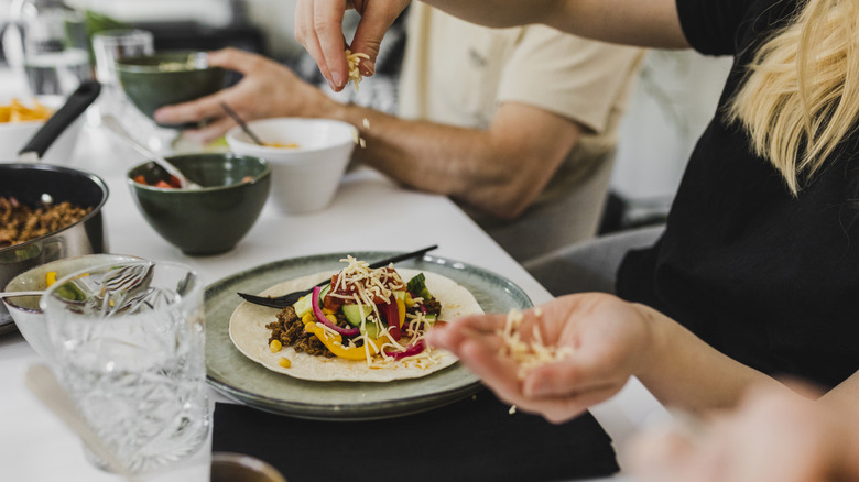 A woman sprinkles cheese onto a homemade taco on a plate