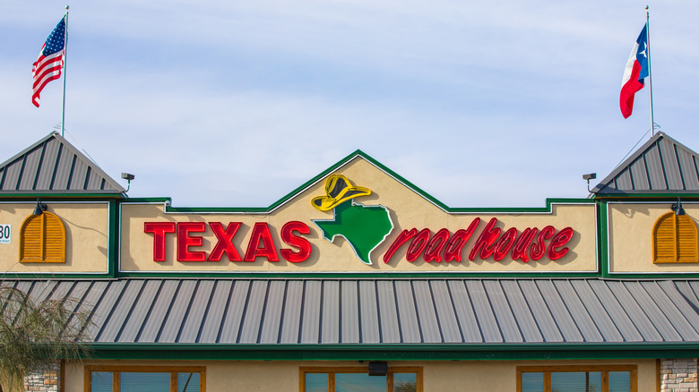 Front of a Texas Roadhouse with U.S. and Texas flags flying, and state of Texas outline as part of logo in its name
