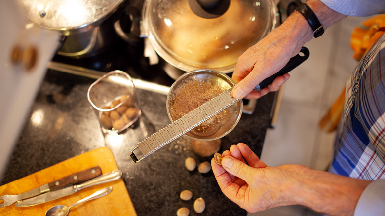 A person grating fresh nutmeg next to a stove