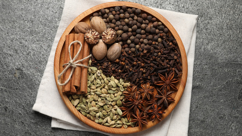 Round tray with whole spices including nutmeg, cinnamon, cardamom, star anise, cloves, and all spice