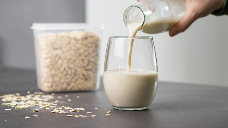 Homemade oat milk being poured into a glass, with oats in the background.