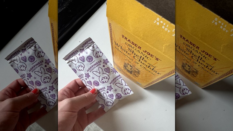 A person is holding an Annie's cheese pouch next to a box of Trader Joe's mac and cheese.