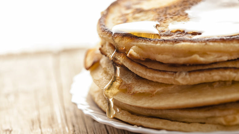 Stack of homemade pancakes with syrup dripping over the side