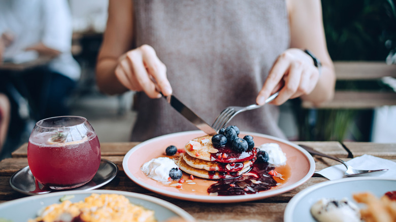 Woman sitting at a restaurant table cutting her brakfast pancakes