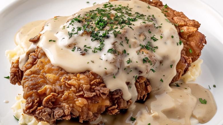 An up-close shot of a country fried steak over mashed potatoes, with gravy and parsley flakes on top