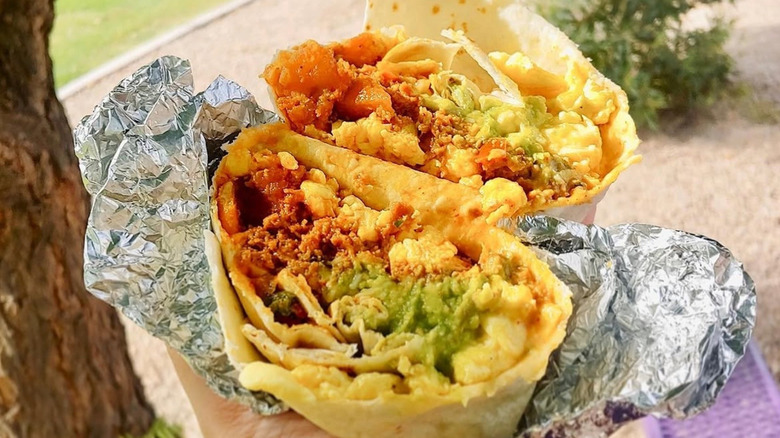 Hand holding a Qdoba breakfast burrito wrapped in foil