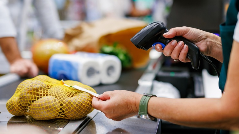 Cashier using barcode scanner to ring up bag of potatoes